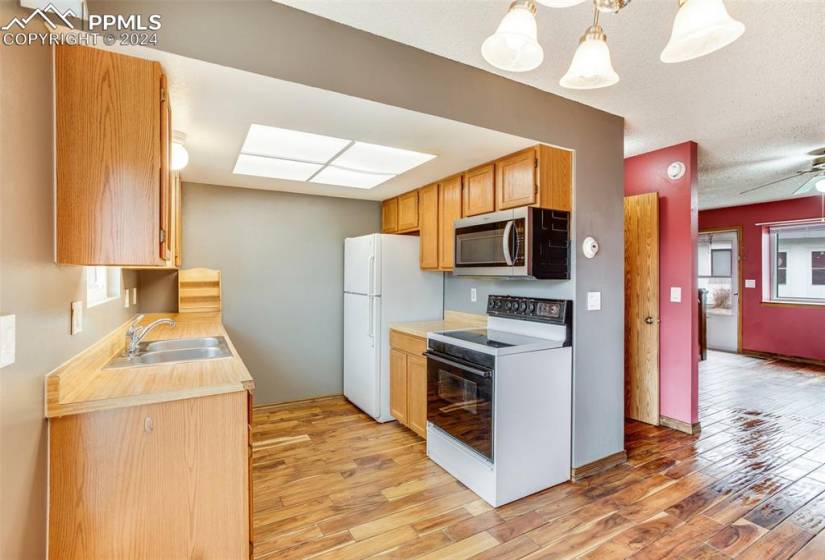 Kitchen featuring ceiling fan, sink, white appliances, light hardwood / wood-style floors, and pendant lighting