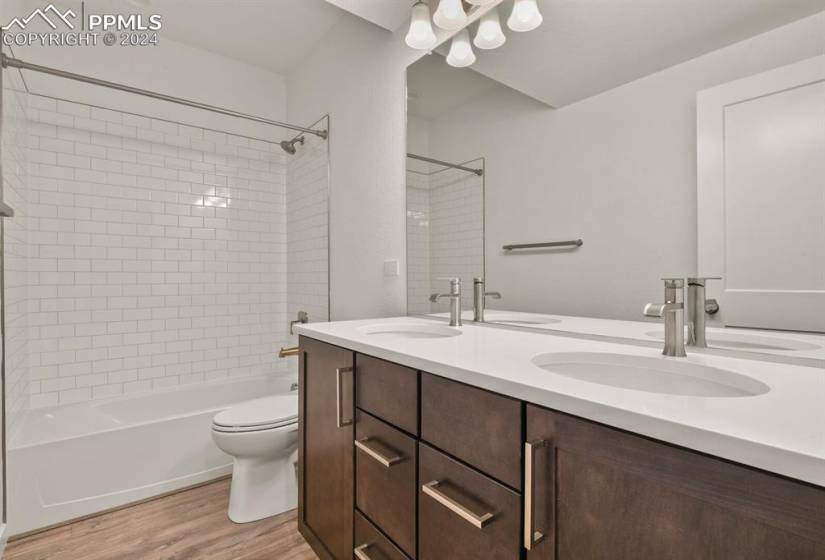 Full bathroom with wood-type flooring, tiled shower / bath combo, toilet, and double sink vanity in basement