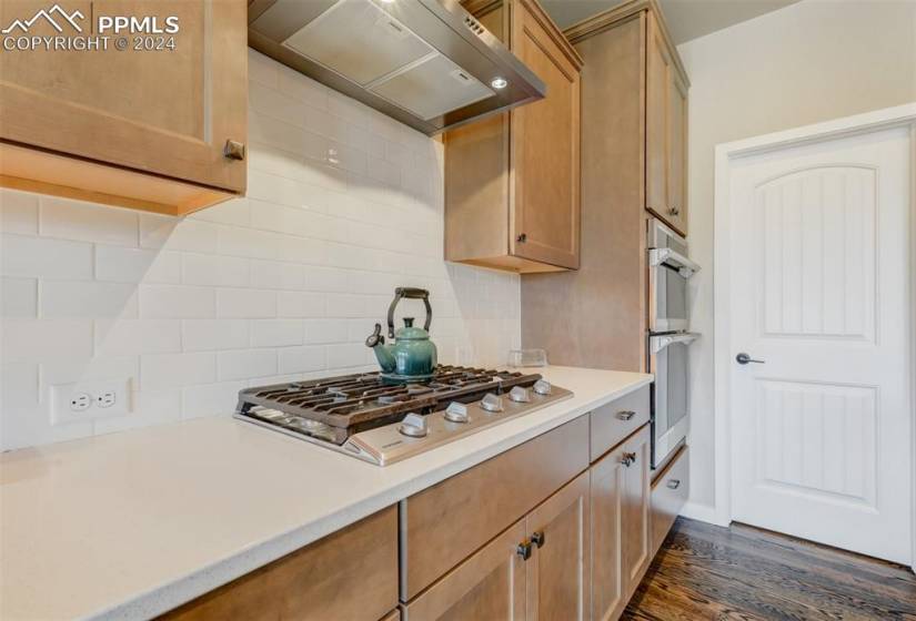 Kitchen featuring appliances with stainless steel finishes, dark hardwood / wood-style floors, tasteful backsplash, and wall chimney exhaust hood