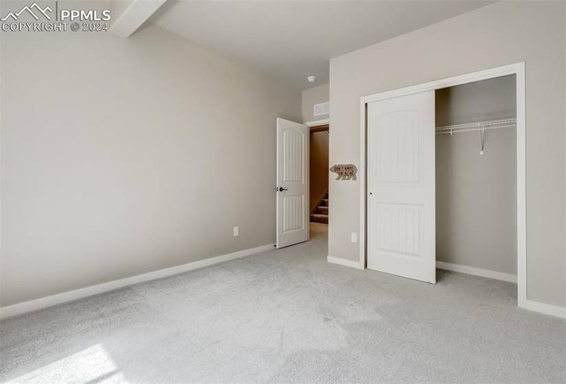 Unfurnished bedroom with carpet flooring, beam ceiling, and a closet