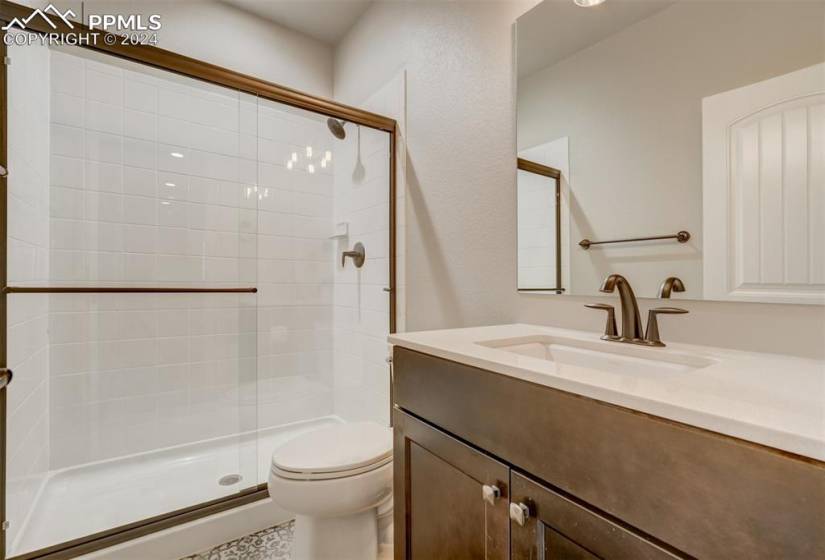Bathroom featuring a shower with door, vanity with extensive cabinet space, and toilet