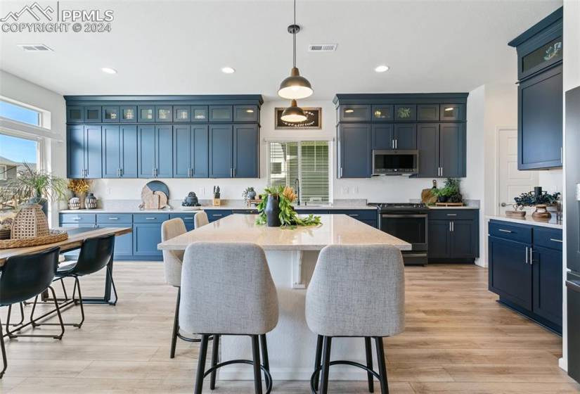 Kitchen with blue cabinets, a kitchen island, range, light hardwood / wood-style floors, and decorative light fixtures