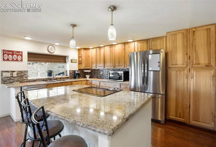 Kitchen with decorative light fixtures, dark hardwood / wood-style flooring, appliances with stainless steel finishes, and a kitchen island all on the main level