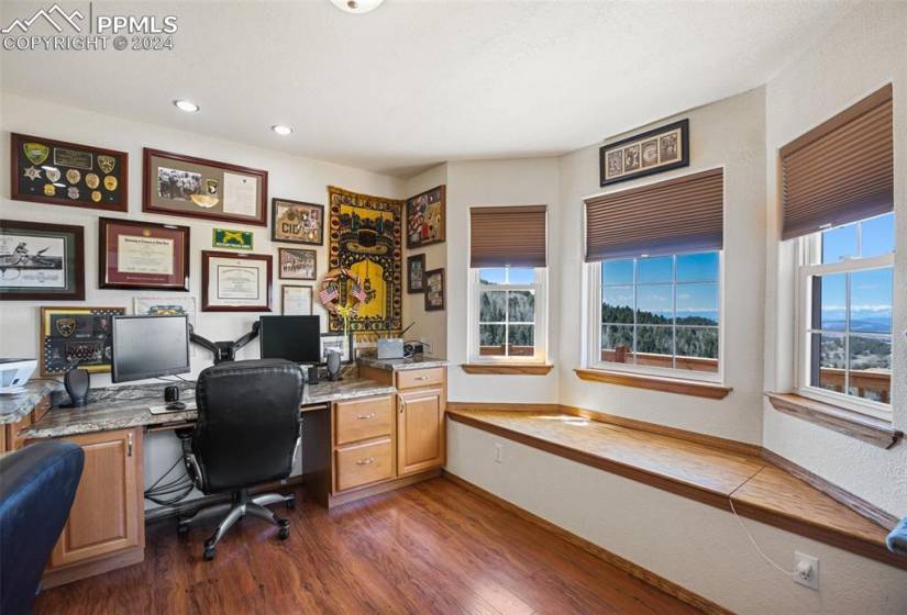 Office space with built in desk and dark hardwood / wood-style flooring and bay window on main level and access to living room