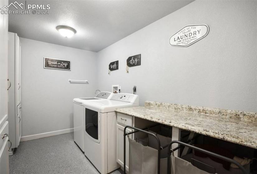 Basement laundry room with washer and dryer, storage, countertop space, rods and epoxy floors