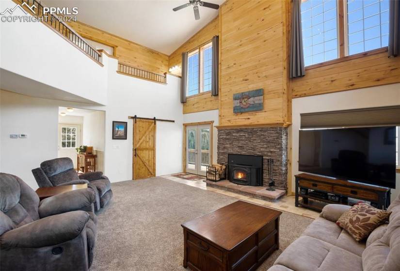 Living room with wooden walls, high vaulted ceiling, carpet floors, a barn door to the office and a stone fireplace all on the main level