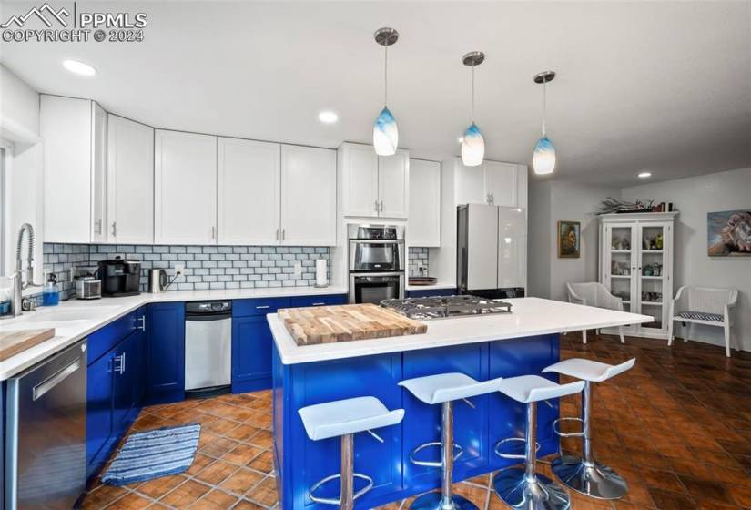 Kitchen featuring blue cabinetry, hanging light fixtures, appliances with stainless steel finishes, a center island, and a breakfast bar