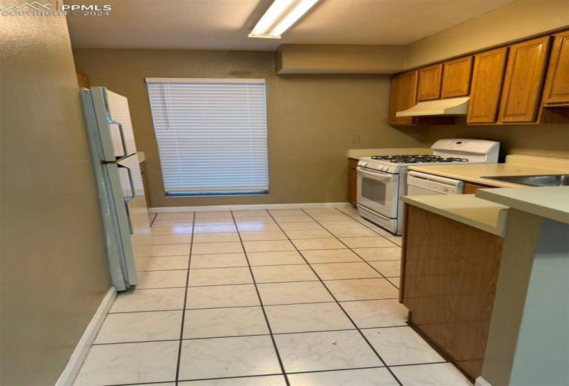 Kitchen featuring sink, stainless steel refrigerator, light tile floors, and custom range hood