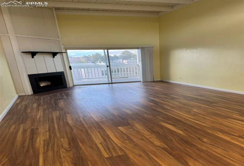 Unfurnished living room featuring wood-type flooring, beam ceiling, and a towering ceiling