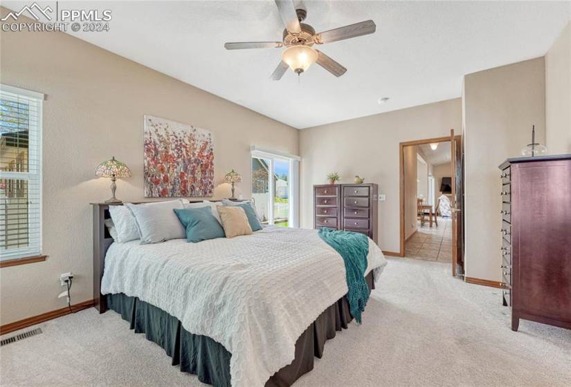 Main Level Primary Owner’s Suite with neutral carpet and lighted ceiling fan off hallway with laundry and pantry.