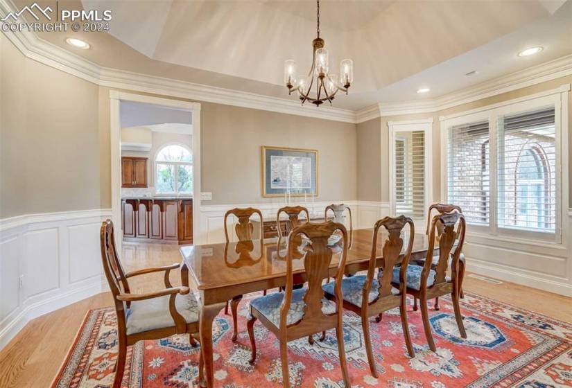 Dining space with light wood-flooring, crown molding, a raised ceiling, and a notable chandelier