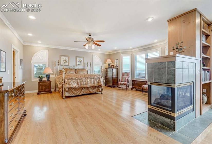 Bedroom with hardwood / wood-floors, crown molding, a tile fireplace, and multiple windows