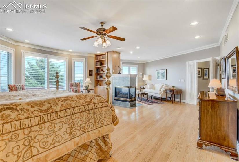 Bedroom featuring light hardwood / wood-floors, ceiling fan, a tile fireplace, and crown molding