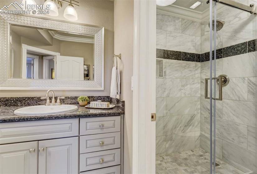 Bathroom with crown molding, a shower with door, and vanity with extensive cabinet space