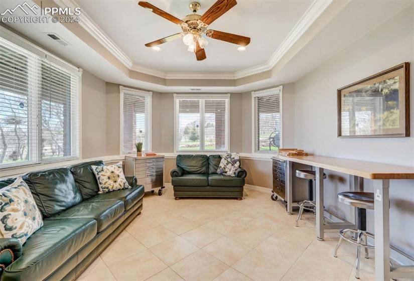 Living room with ceiling fan, a tray ceiling, light tile floors, and ornamental molding