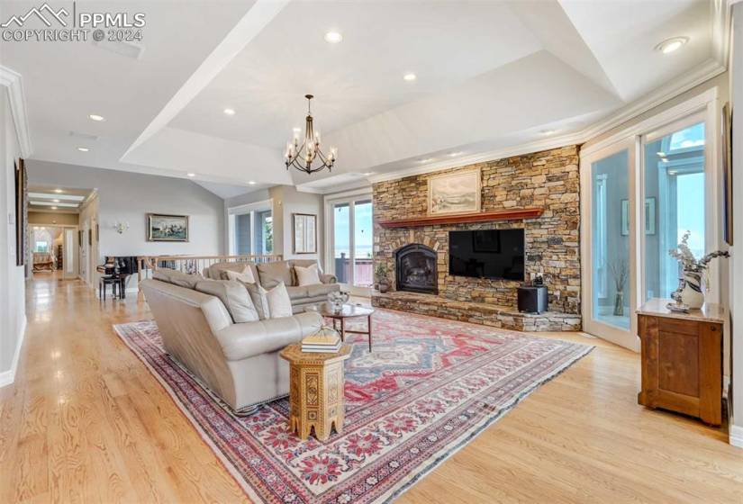 Living room with light hardwood / wood-floors, crown molding, a tray ceiling, a fireplace, and a chandelier