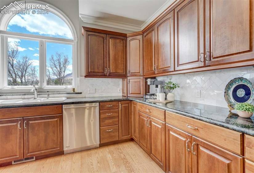 Kitchen with light hardwood / wood-flooring, backsplash, sink, dark stone counters, and dishwasher