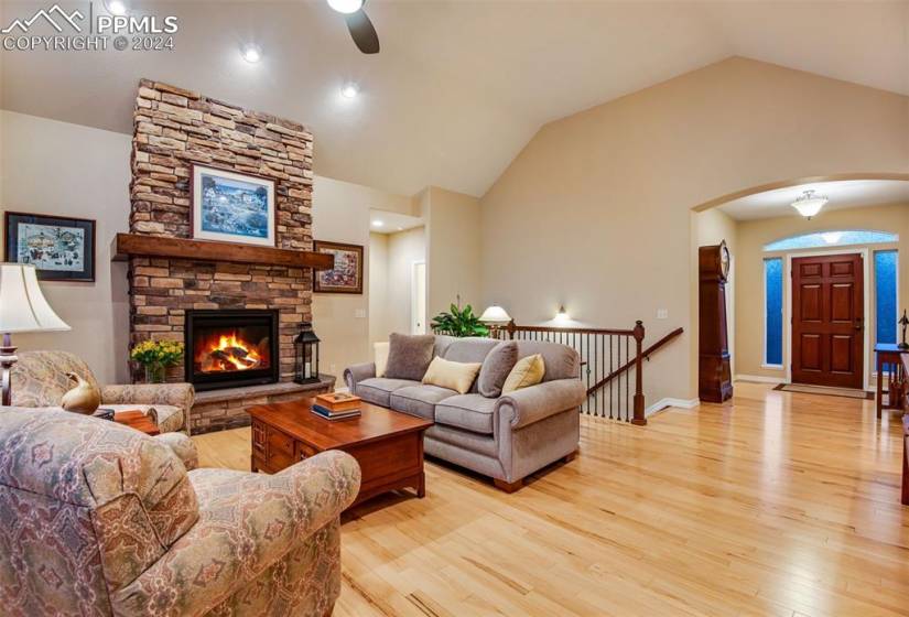 Living room featuring vaulted ceiling, ceiling fan, light hardwood / wood-style floors, and a fireplace