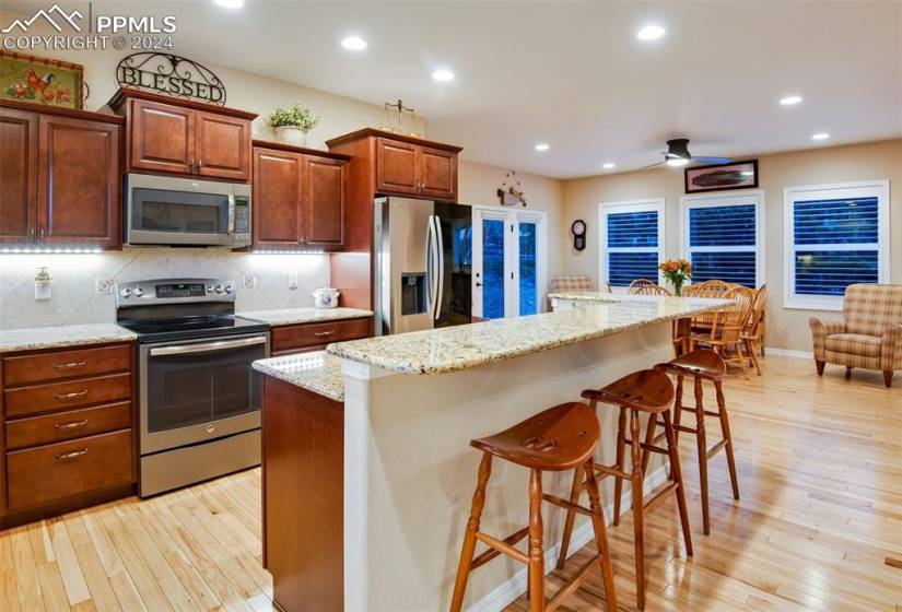 Kitchen with a kitchen breakfast bar, light hardwood / wood-style flooring, appliances with stainless steel finishes, tasteful backsplash, and ceiling fan