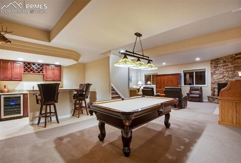 Playroom featuring light colored carpet, a stone fireplace, pool table, and beverage cooler