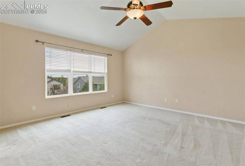 Empty room with ceiling fan, vaulted ceiling, and carpet floors