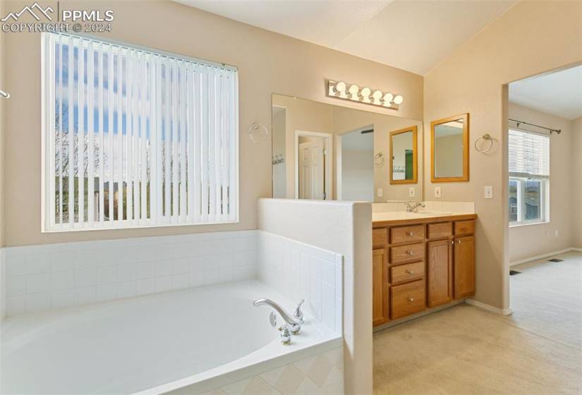 Bathroom with vanity with extensive cabinet space, tiled tub, and lofted ceiling