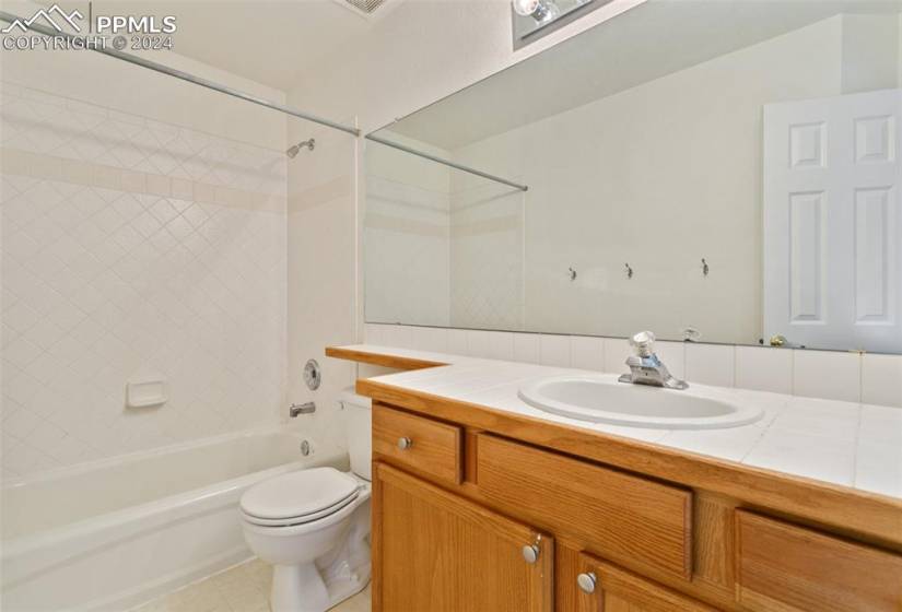 Full bathroom featuring tile flooring, toilet, large vanity, and tiled shower / bath