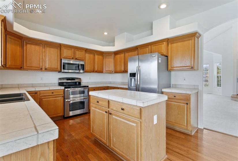 Kitchen with a center island, tile counters, wood-type flooring, appliances with stainless steel finishes, and sink