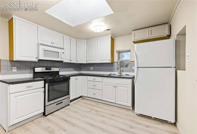Kitchen with light hardwood / wood-style floors, white appliances, tasteful backsplash, sink, and a skylight
