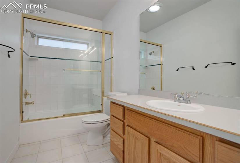 Full main level bathroom with tile flooring, shower / bath combination with glass door, toilet, and large vanity
