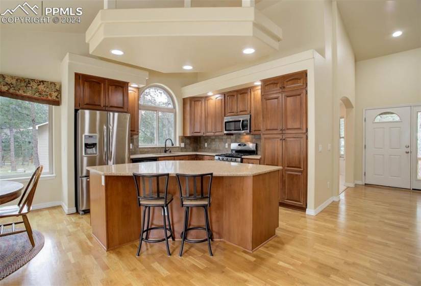 Kitchen with a towering ceiling, light hardwood flooring, stainless steel appliances, backsplash, and a center island