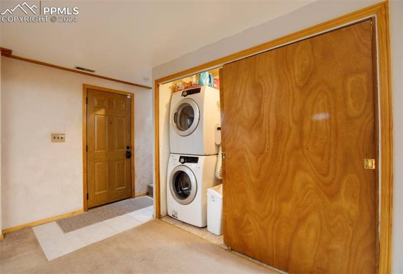 Laundry room with stacked washer and clothes dryer and light tile floors