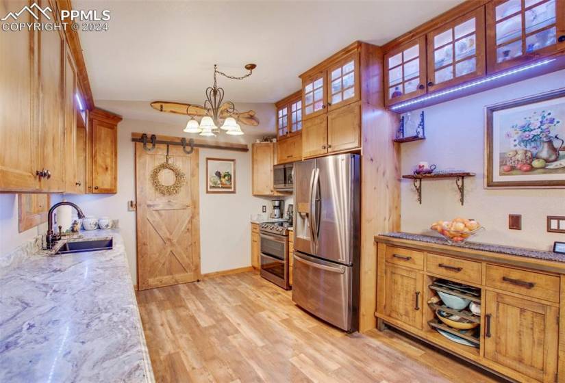 Kitchen with light wood-type flooring, a notable chandelier, hanging light fixtures, sink, and appliances with stainless steel finishes