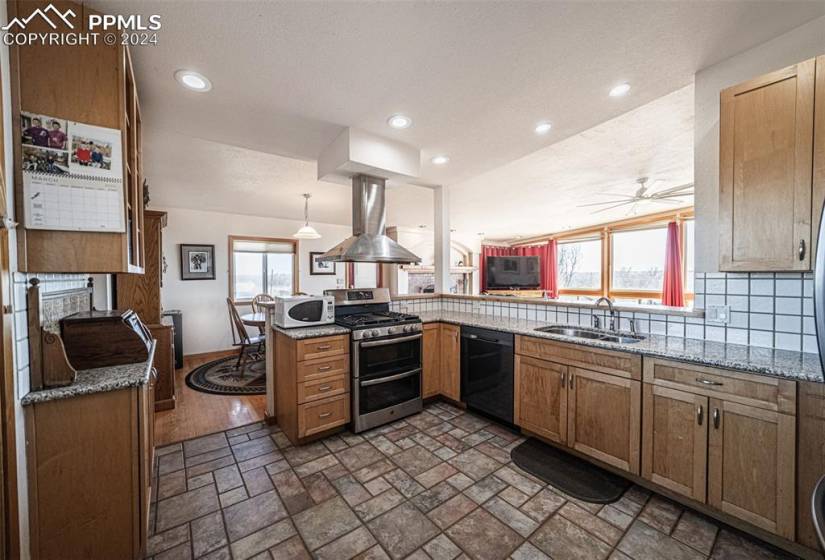 Kitchen featuring ceiling fan, island range hood, range with two ovens, sink, and black dishwasher