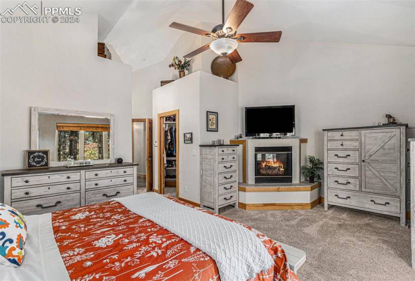 Carpeted bedroom with a tiled fireplace, a closet, ceiling fan, a spacious closet, and high vaulted ceiling