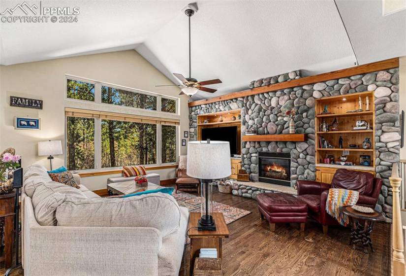 Living room featuring a textured ceiling, lofted ceiling, a fireplace, hardwood / wood-style flooring, and ceiling fan