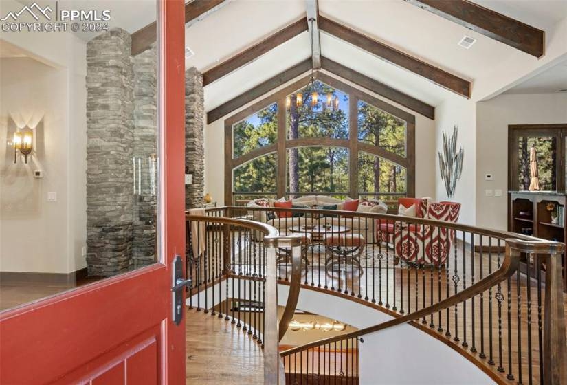 Front entry, living room, vaulted beam ceiling, wood flooring and curved staircase into basement.