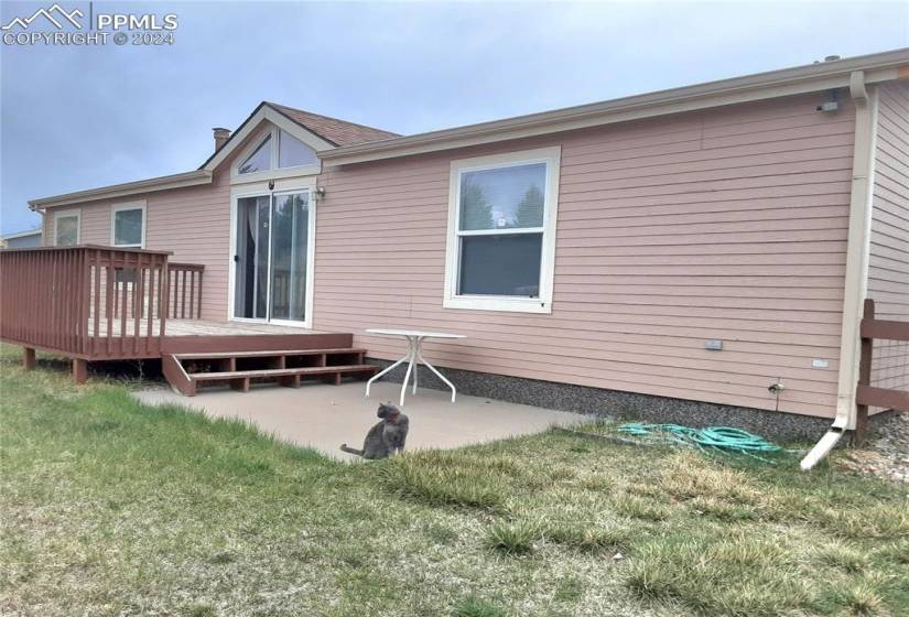 Back of property with a wooden deck, a patio area, and a lawn