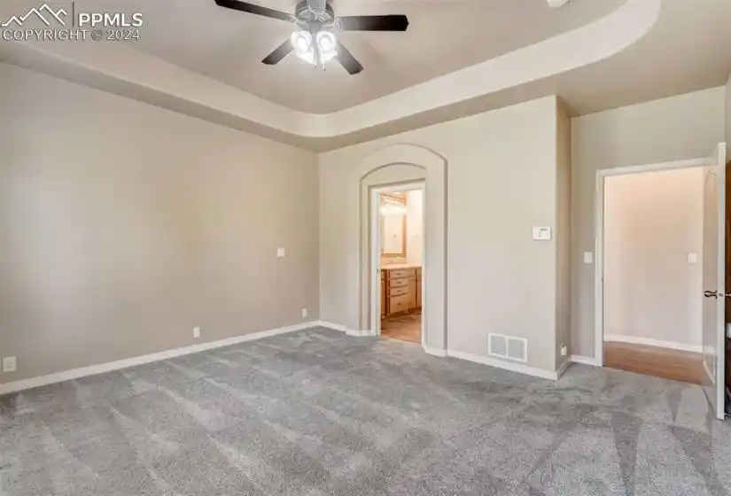 Unfurnished bedroom with carpet flooring, ceiling fan, and a raised ceiling