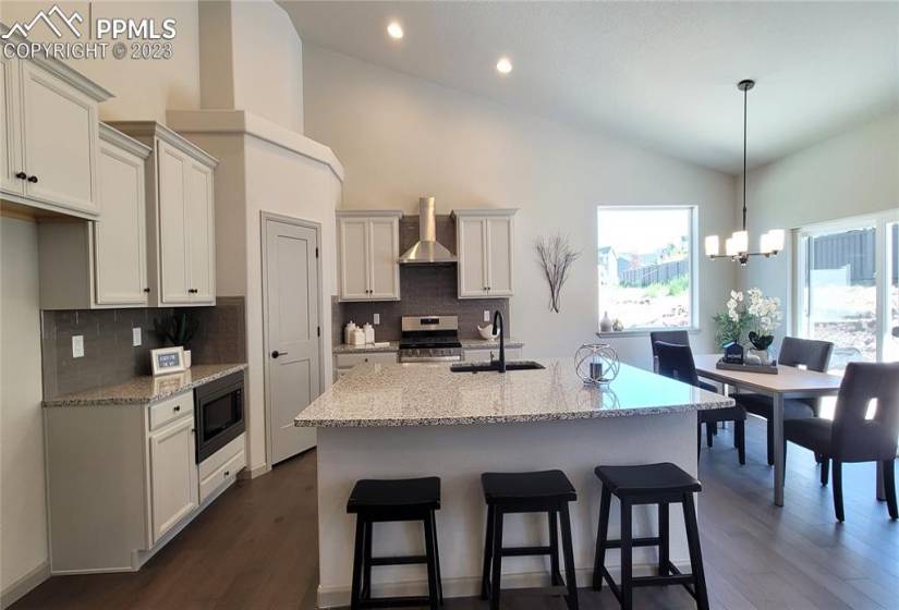 Grand Kitchen with granite slab counters, staggered cabinets, pantry, large island providing additional seating, and stainless steel gas range, pyramid hood, microwave, and dishwasher!