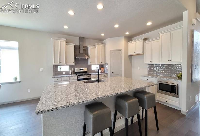 Kitchen with Granite Slab Counters, Staggered Cabinets, Pantry, Large Island providing additional seating, and stainless steel pyramid hood, gas range, microwave, and dishwasher!
